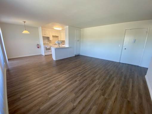 an empty living room with wood flooring and a kitchen