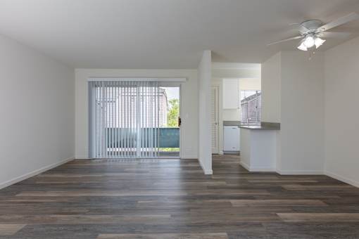 an empty living room and kitchen with wood flooring and a ceiling fan