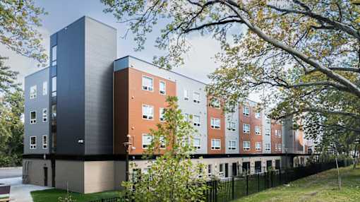 A modern building with a black and brown exterior is surrounded by trees and other buildings.