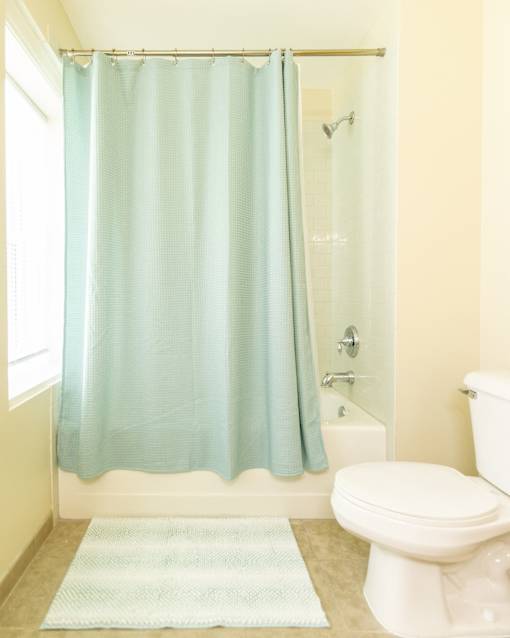 Bathroom area of an apartment fitted with tiled flooring, a shower, a toilet, and high ceiling.