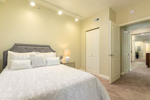Bedroom in an apartment furnished with a queen-size bed, a nightstand, carpet flooring, closet, and high ceiling.