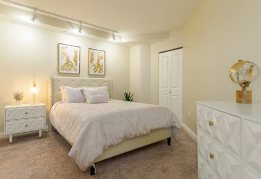 Bedroom in an apartment furnished with a queen-size bed, a nightstand, carpet flooring, and a high ceiling.