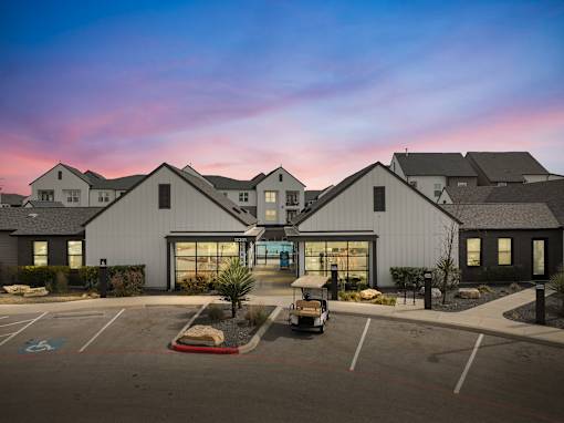 A parking lot in front of a building with a golf cart parked in the lot.