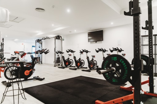 a gym with various bikes and weights on the floor and a television on the wall