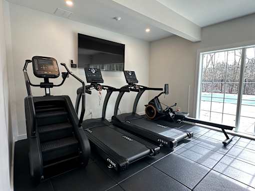 A black treadmill and a black stair climber are in a room with a large window.