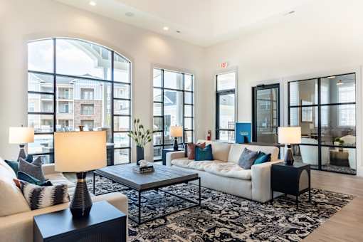 A well-lit living room with a large window, a sofa, a coffee table, and a side table with a lamp.