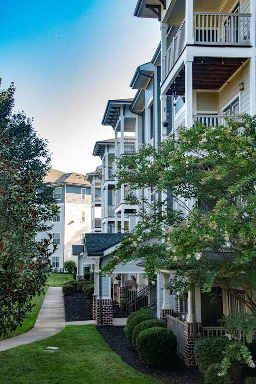 A white building with a balcony and a tree in front of it.