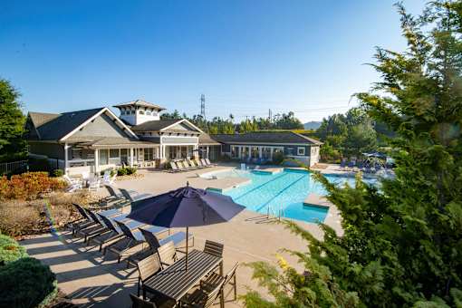 A large swimming pool with a blue umbrella and chairs around it.