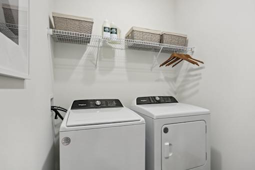A laundry room with a washer and dryer and a shelf with baskets and a handbag. at Arcadia Cartersville Apartments, Cartersville, GA