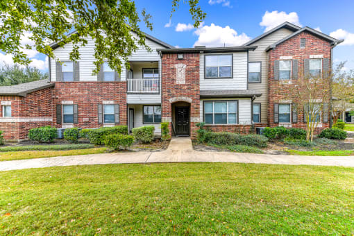 front view of an apartment building with green grass and trees at Artesian on Westheimer, Texas