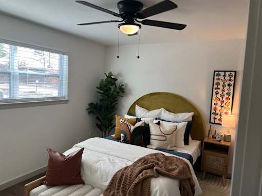 A bedroom with a bed, a ceiling fan, and a plant.at Century Apartments, Memphis Tennessee  