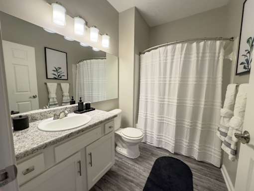 A bathroom with a white toilet, sink, and shower curtain at Enclave at Wolfchase Apartments, Tennessee 38016