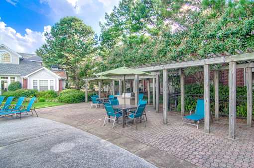 A patio with blue chairs and a table is surrounded by trees at Enclave at Wolfchase Apartments, Memphis