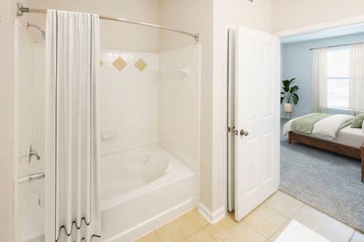 A white bathroom with a walk-in shower and a bedroom in the background.