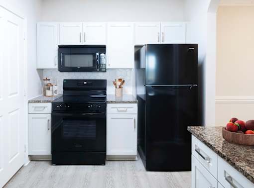 A black refrigerator stands in a kitchen with white cabinets and a black oven.