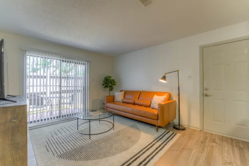a living room with an orange couch and a sliding glass door at Brightwaters Apartments, Little Rock, Arkansas