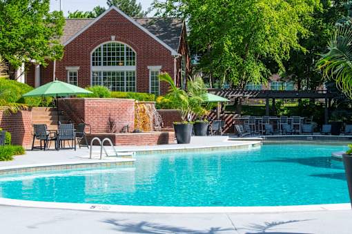 A pool in front of a house with a green umbrella.