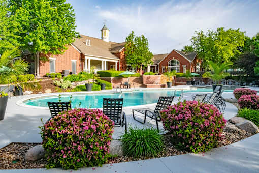 A pool surrounded by a garden with a house in the background.
