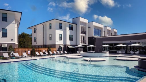 a large swimming pool with lounge chairs and umbrellas in front of a building at Esplanade District Apartments, Little Rock