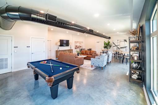 A pool table is in the middle of a room with a long black pipe on the ceiling.
