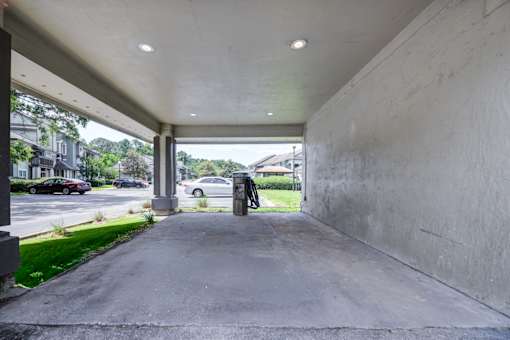A concrete covered walkway with a parking lot and trees in the background.
