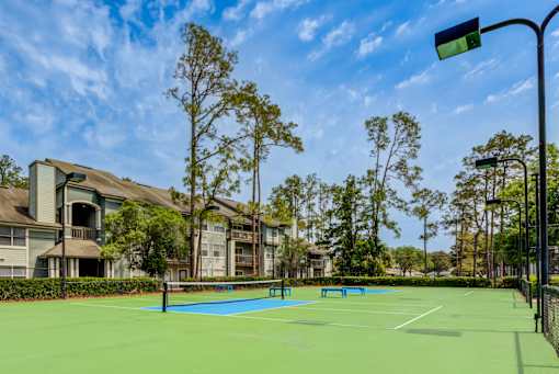 A tennis court is surrounded by trees and buildings.