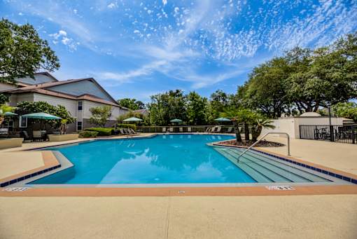 A large outdoor swimming pool surrounded by trees and a house.