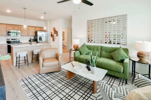 A living room with a green couch, a coffee table, and a kitchen area in the background.