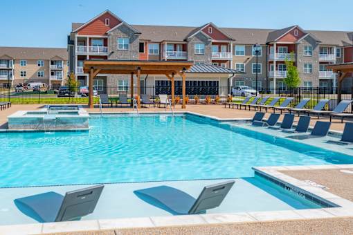 A pool with sun loungers and a building in the background. at Grays Creek Apartments, Cordova