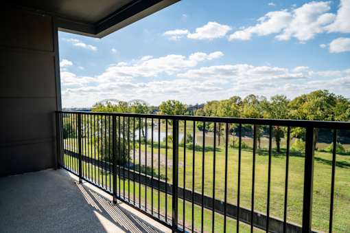 A balcony with a black railing overlooks a green lawn and trees at Harbor Side at Conwood Flats Apartments in Uptown Memphis, TN