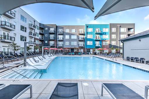 A large outdoor swimming pool surrounded by lounge chairs and umbrellas at Highland Row Apartments, Memphis, Tennessee