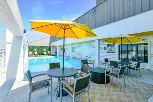 A poolside area with a table and chairs under a yellow umbrella.