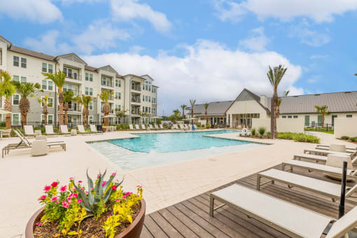 a swimming pool with lounge chairs and a potted plant in front of an apartment building at The Livano Kemah, Kemah, TX, 77565