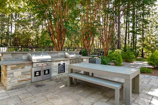 A stone barbecue area with a bench and a grill. at Manchester at Mansell, Roswell 