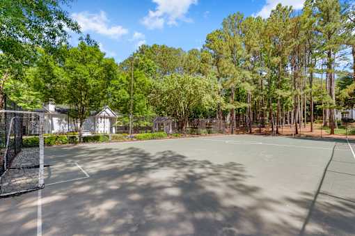 A tennis court surrounded by trees and a building in the background. at Manchester at Mansell, Roswell Georgia 