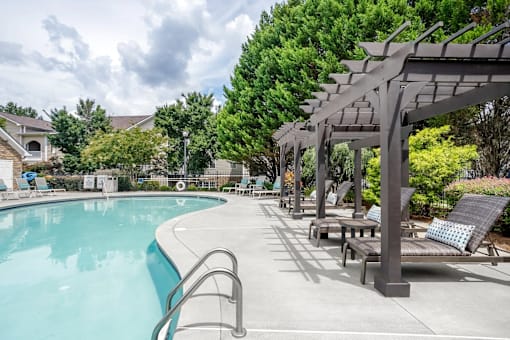 A pool with a metal ladder and a pergola with cushioned seating.