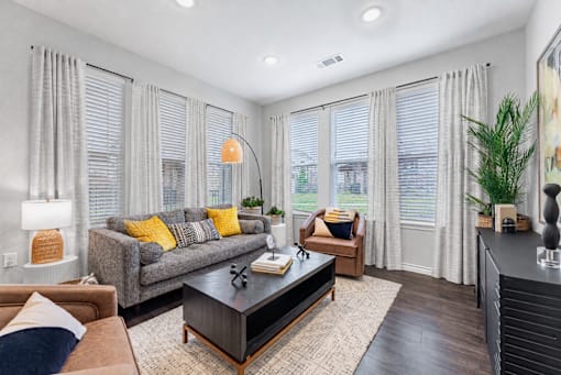 A living room with a grey couch, a brown armchair, a coffee table, and a large window with curtains.