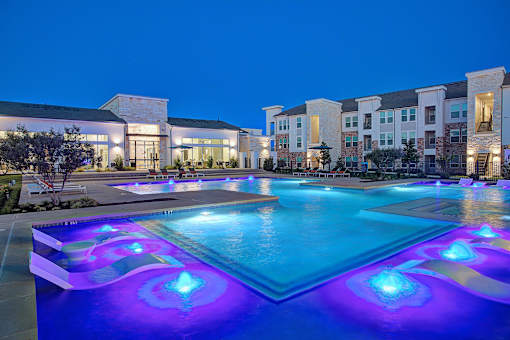 A swimming pool with blue and purple lights in front of a building.