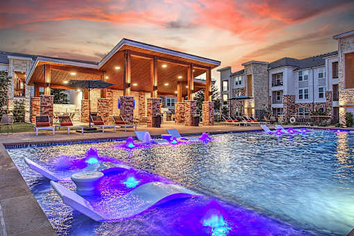 A pool with a waterfall and lights in the middle of it.