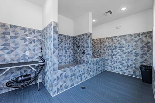 A bathroom with a blue tiled shower and a black trash can.