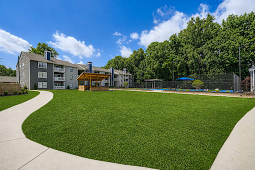 A grassy area in front of a building with a fence and trees in the background.