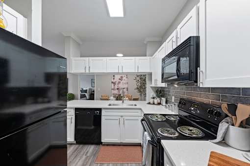 Modern kitchen with black appliances and white cabinets at The Ambrose, Texas, 77040