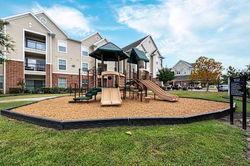 A playground with a slide and sandbox in front of apartment buildings at The Fenwick Apartments, Humble, TX