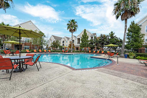 A pool surrounded by chairs and umbrellas with houses in the background at The Fenwick Apartments, Texas