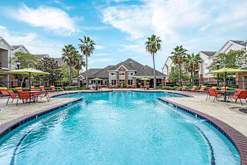 A large swimming pool in a residential area with red lounge chairs and umbrellas at The Fenwick Apartments, Humble, Texas