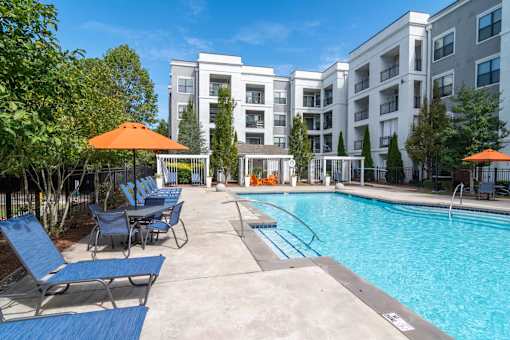 A swimming pool surrounded by chairs and umbrellas in front of a building. at The Ren, Atlanta, GA