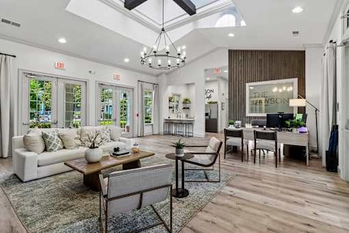 A well-lit, spacious living room with a white sofa, wooden coffee table, and a chandelier.