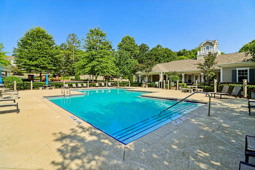 A large swimming pool surrounded by trees and a building in the background.