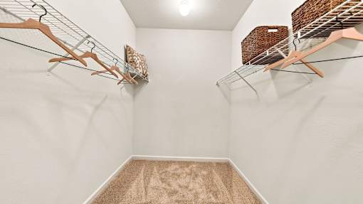 A walk in closet with a carpeted floor and clothes hanging on racks.