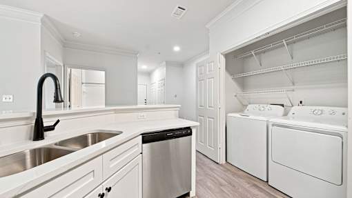 A white kitchen with a black faucet and a black trash bin.